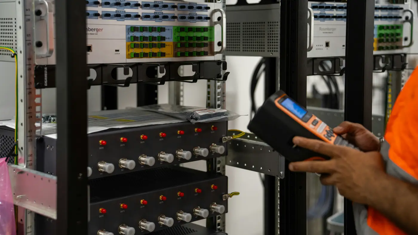 Technician inspecting a fibre patch panel rack with a handheld diagnostic tool